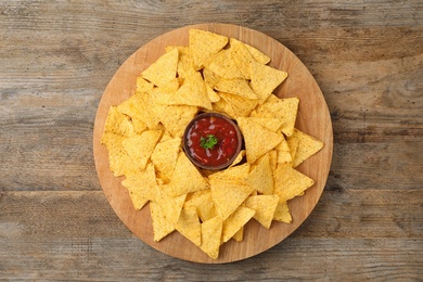 Board with Mexican nacho chips and sauce on wooden background, top view