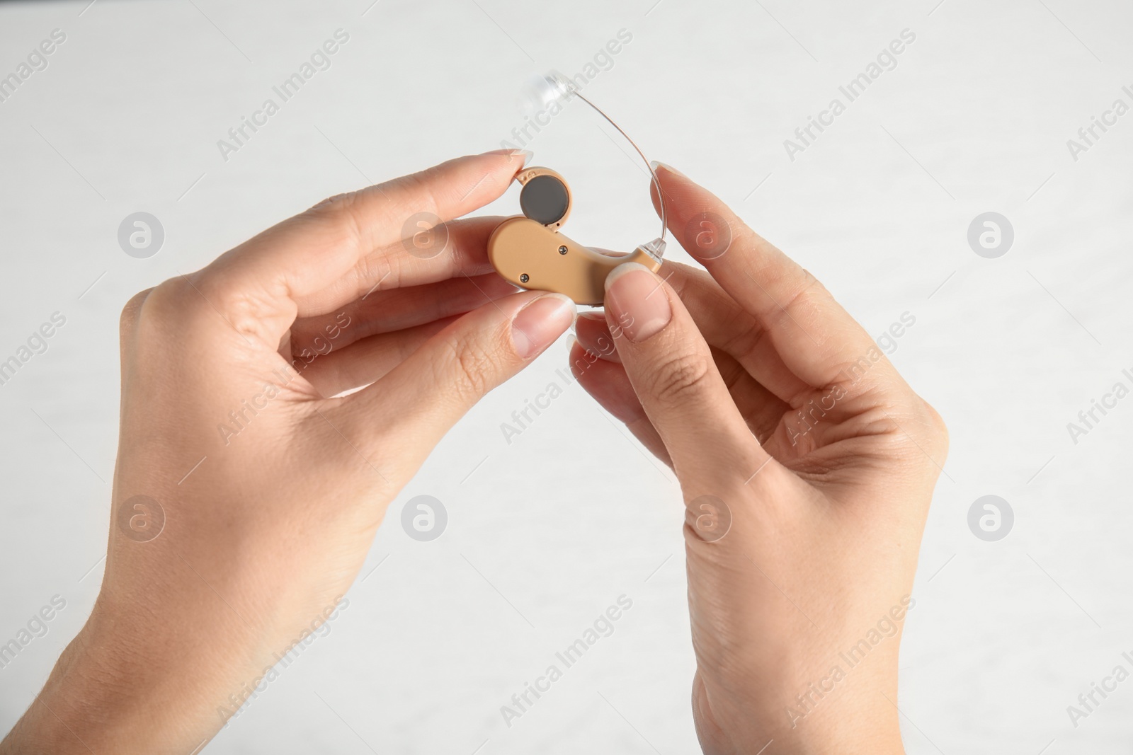 Photo of Woman putting battery into hearing aid on light background, closeup