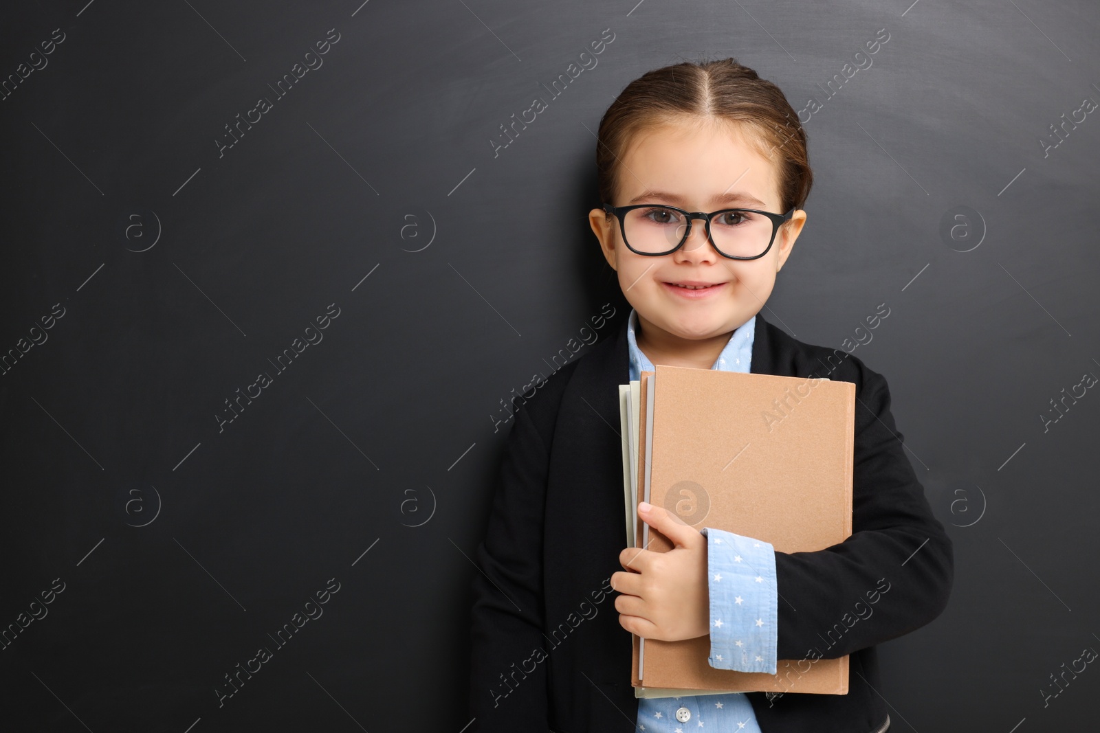 Photo of Happy little school child with books near chalkboard. Space for text