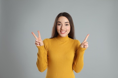 Photo of Woman in yellow turtleneck sweater showing number three with her hands on grey background