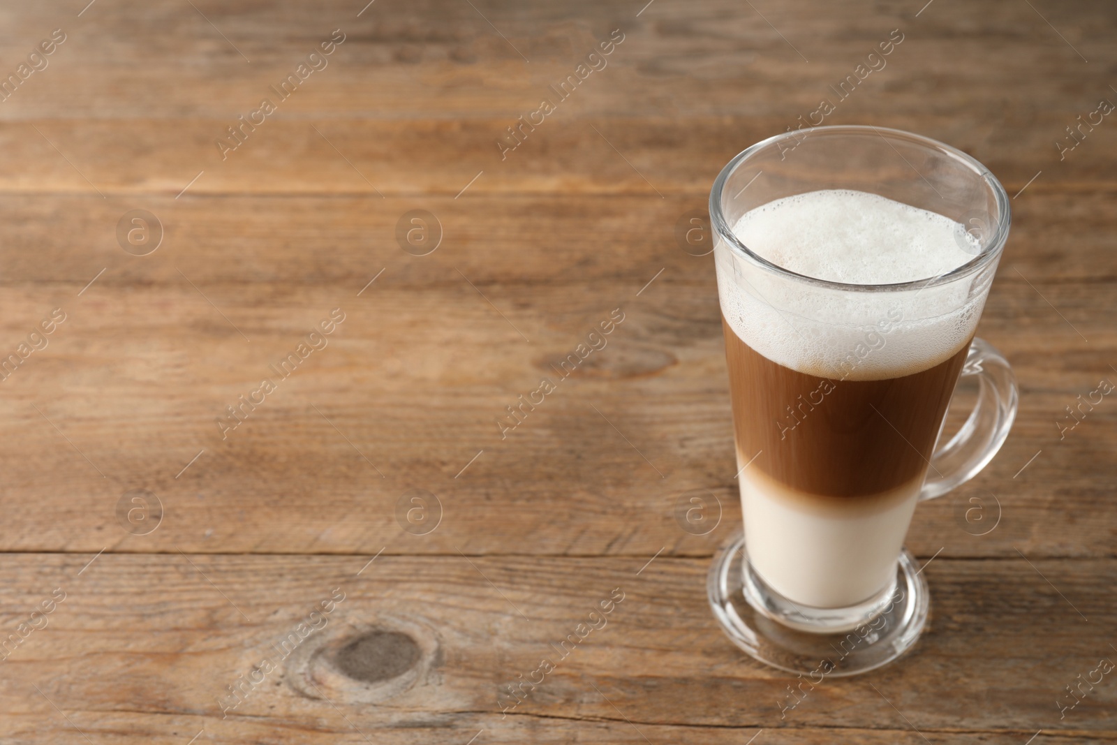 Photo of Hot coffee with milk in glass cup on wooden table. Space for text