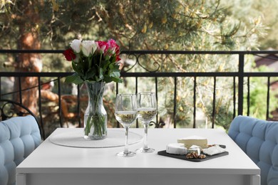 Photo of Beautiful roses, glasses of wine and snacks on white table at balcony