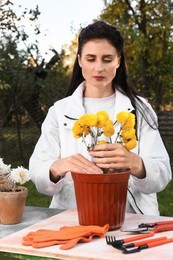 Woman transplanting flowers into pot at table outdoors