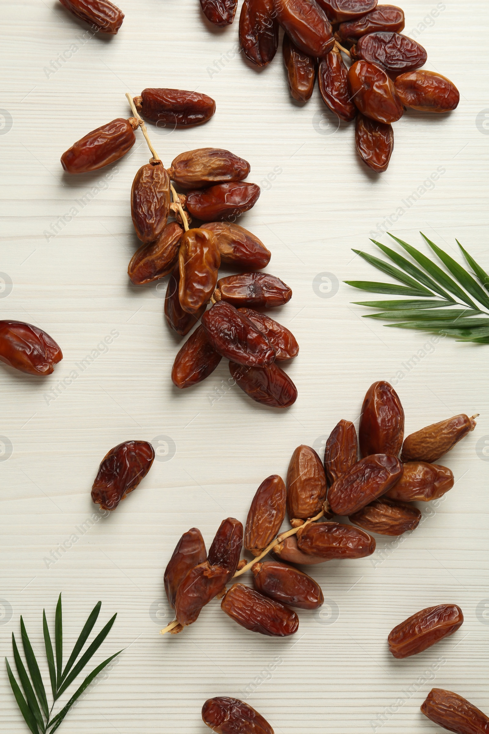 Photo of Sweet dried dates and green leaves on white wooden table, flat lay