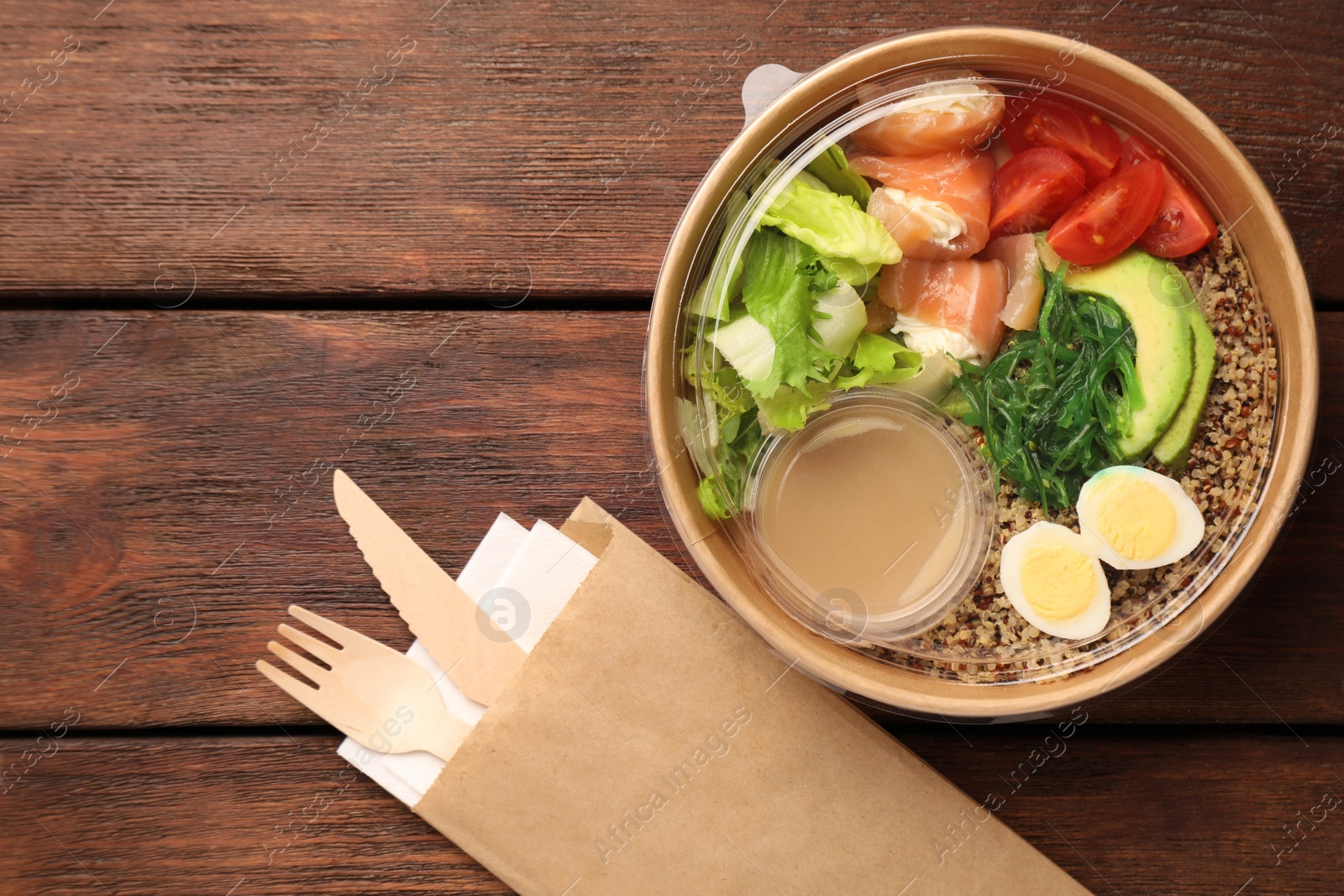 Photo of Tasty food in container with knife and fork on wooden table, flat lay. Space for text