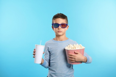 Boy with 3D glasses, popcorn and beverage during cinema show on color background