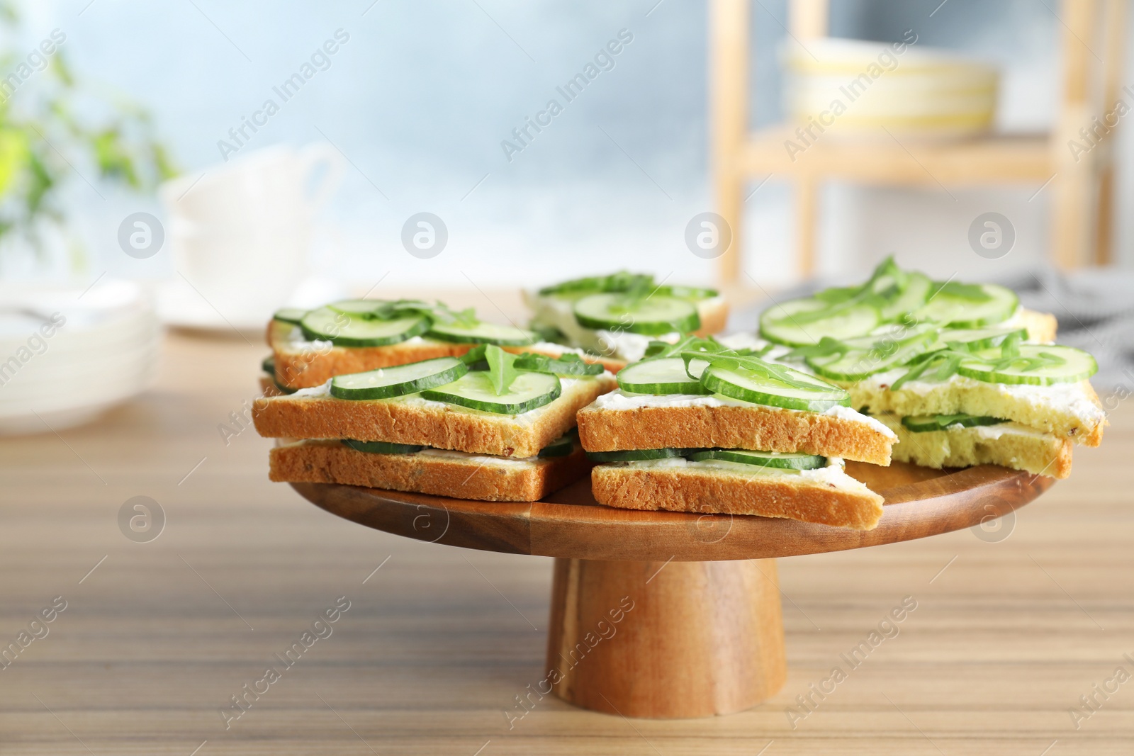 Photo of Wooden stand with traditional English cucumber sandwiches on table