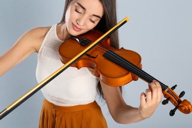 Beautiful woman playing violin on grey background, closeup