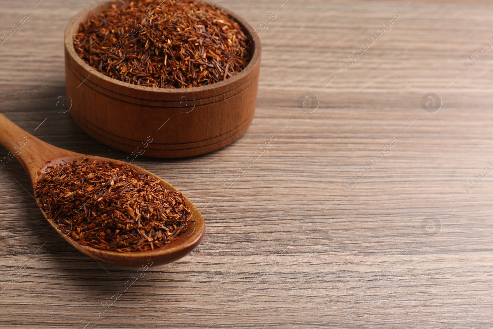 Photo of Spoon and bowl with dry rooibos leaves on wooden table, space for text