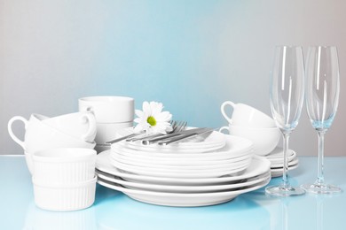 Photo of Set of clean dishes, glasses and cutlery on light blue table