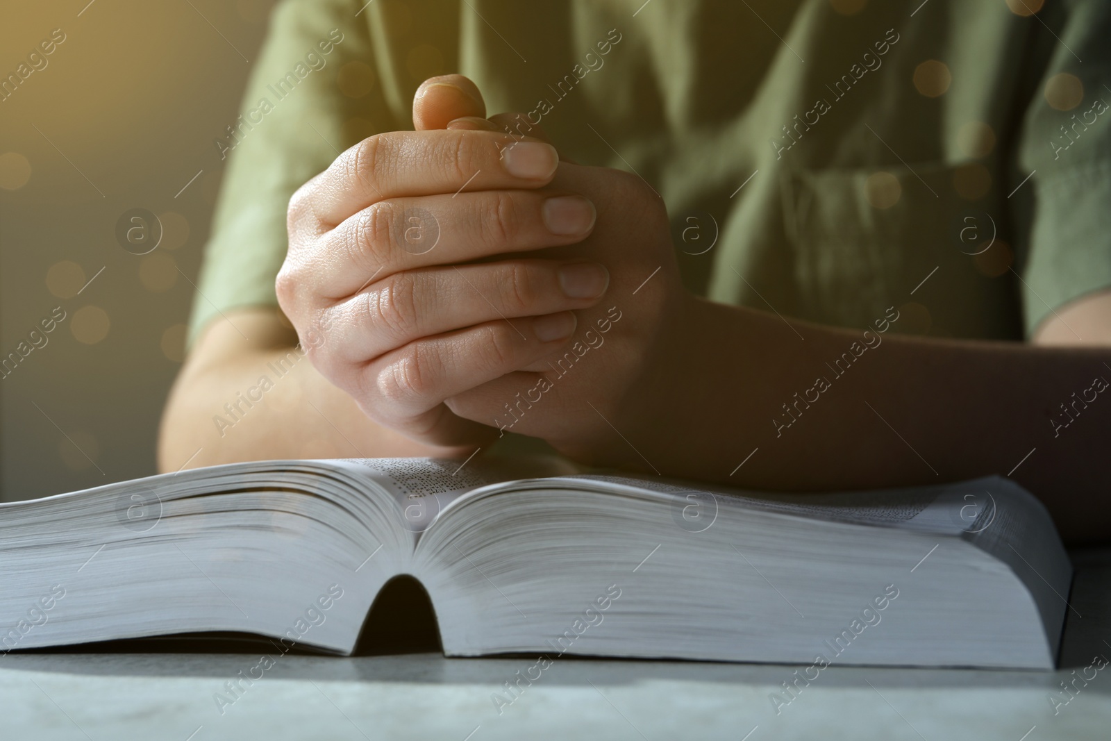 Photo of Woman holding hands clasped while praying over Bible at grey textured table, closeup