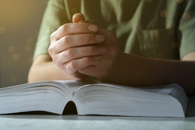 Photo of Woman holding hands clasped while praying over Bible at grey textured table, closeup