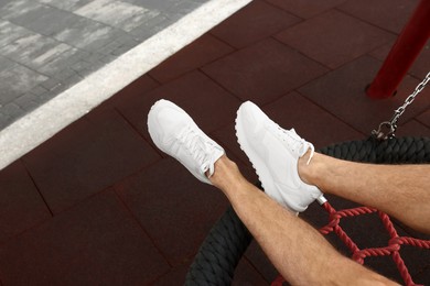 Man in stylish sneakers sitting on swing outdoors, above view. Space for text