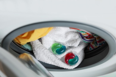 Photo of Laundry detergent capsules and clothes in washing machine drum, closeup view