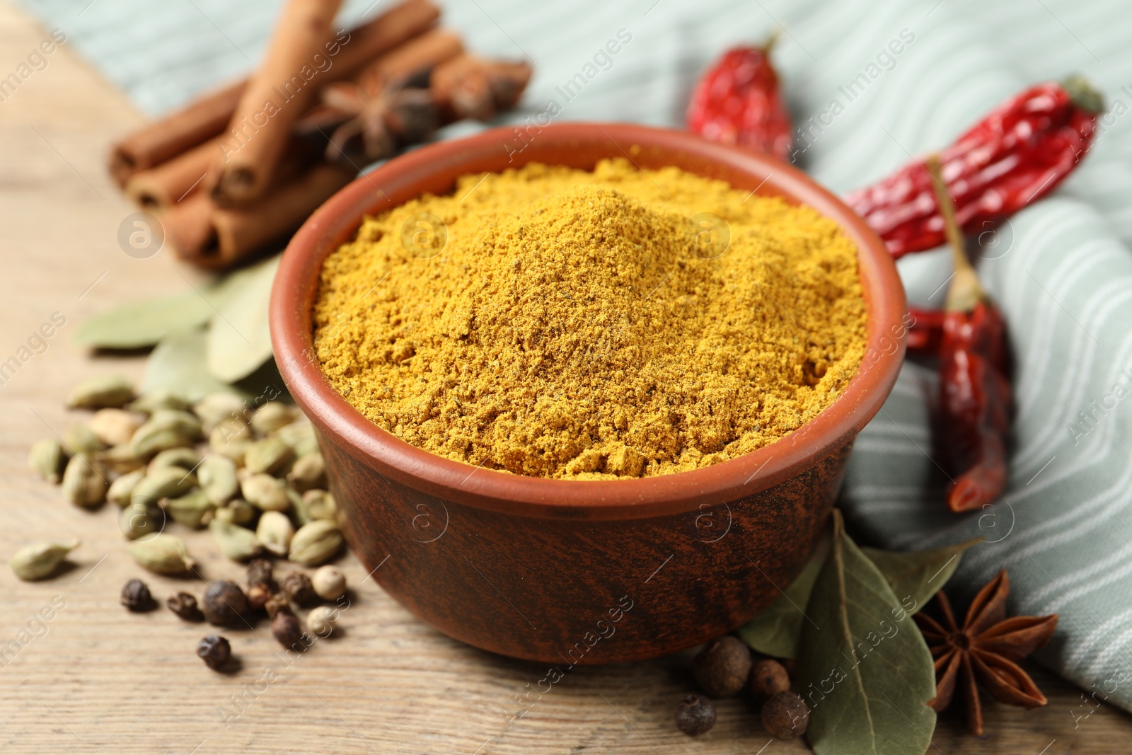 Photo of Curry powder in bowl and other spices on wooden table, closeup