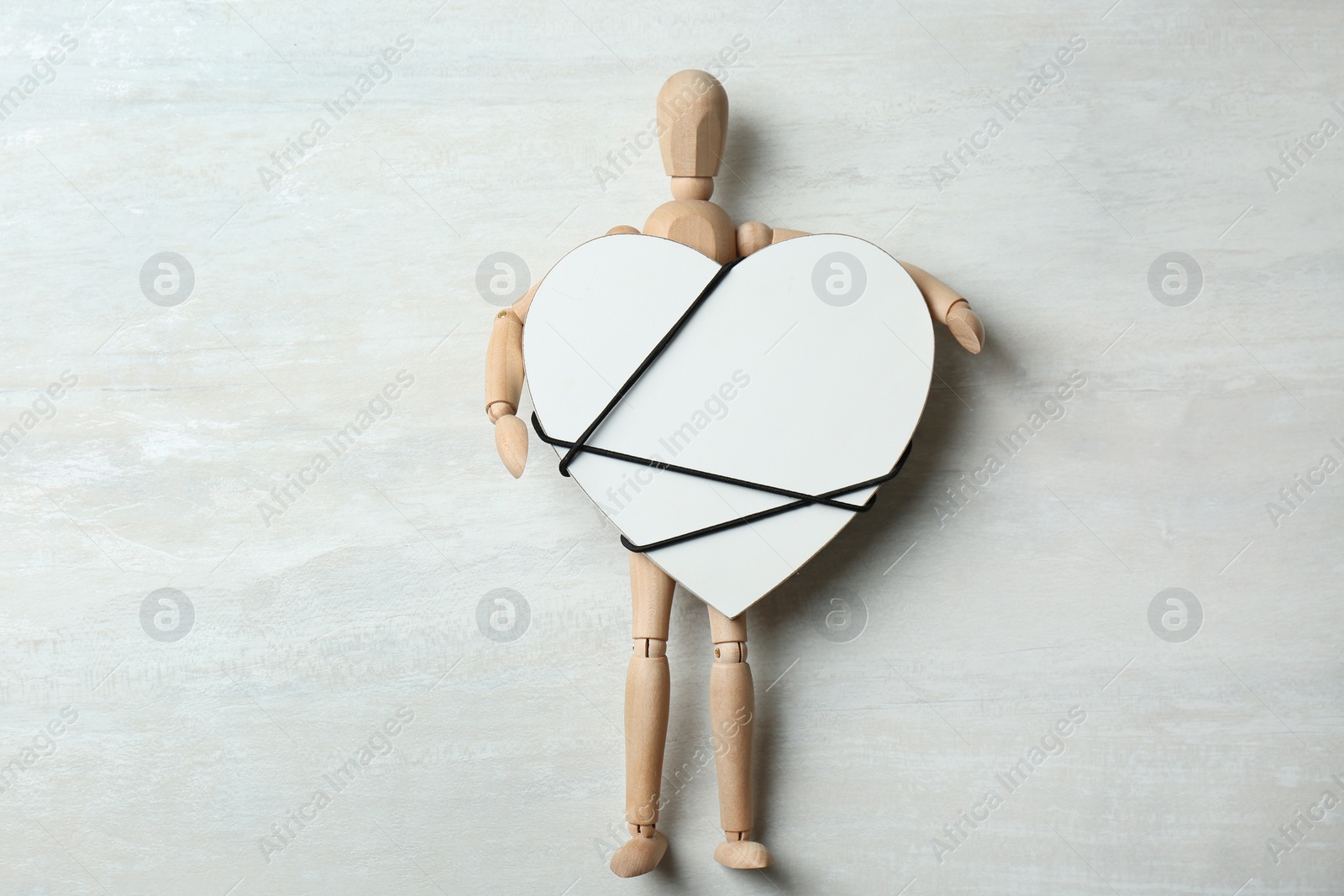 Photo of Wooden puppet holding heart tied with cord on gray background, top view. Relationship problems
