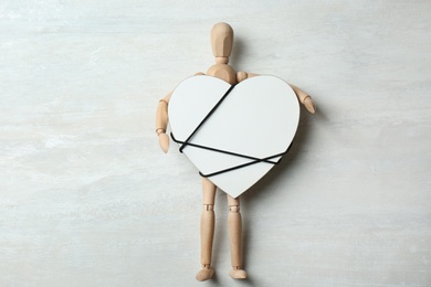 Wooden puppet holding heart tied with cord on gray background, top view. Relationship problems