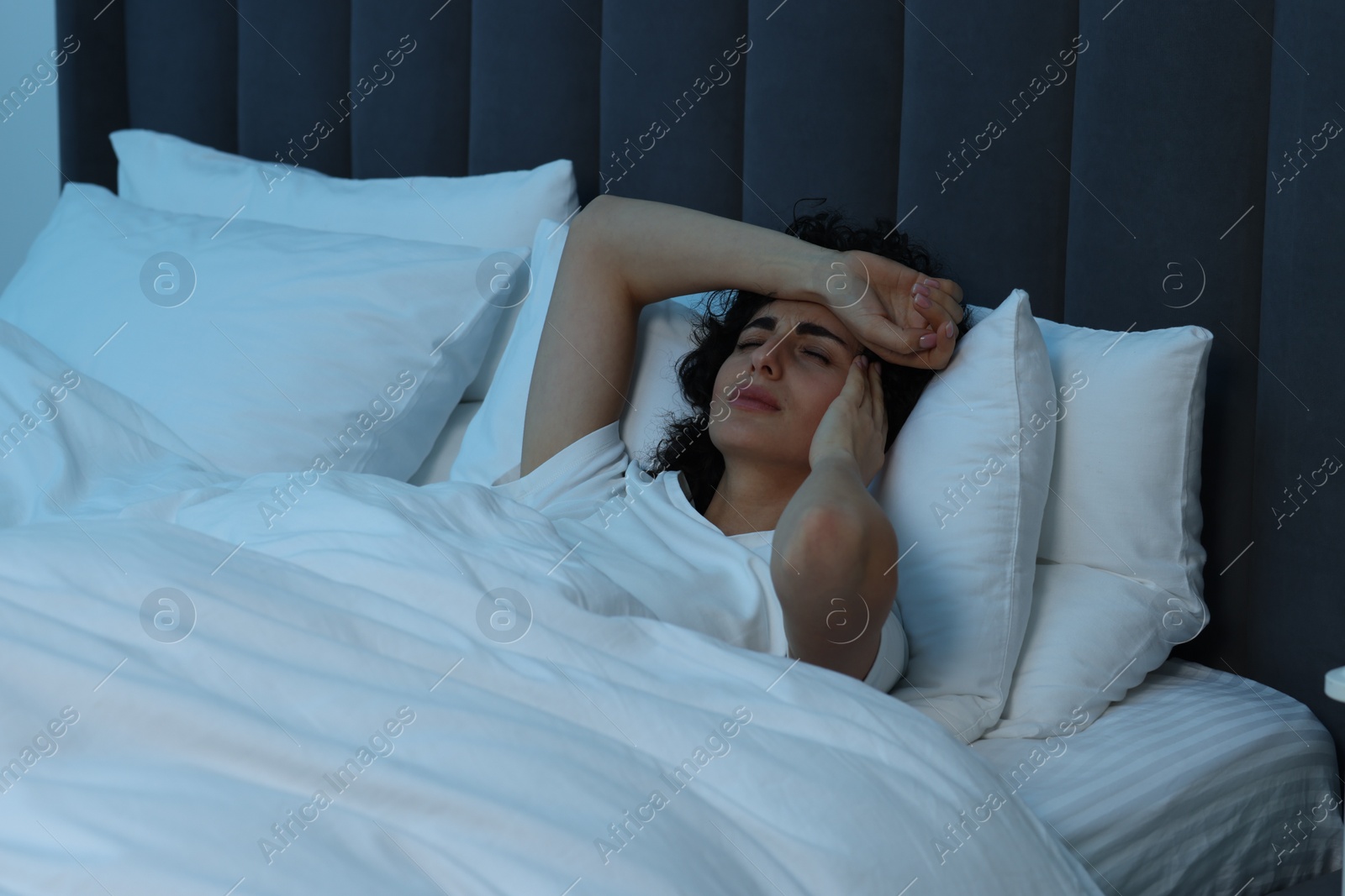 Photo of Young woman suffering from headache in bed at night