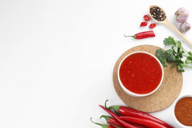 Photo of Spicy chili sauce in bowl and ingredients on white background, flat lay. Space for text