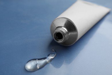 Photo of Open white tube with ointment on blue background, closeup