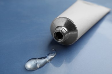 Open white tube with ointment on blue background, closeup