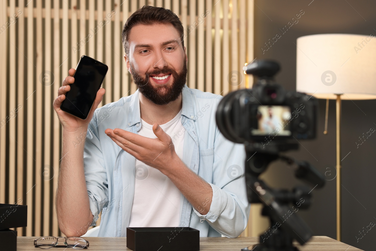 Photo of Smiling technology blogger with smartphone recording video review at home