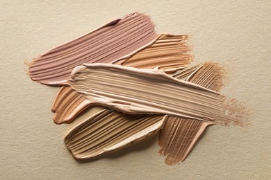 Different shades of liquid foundation on beige background, top view