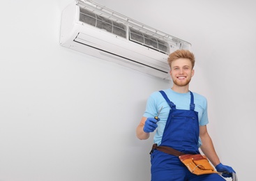 Professional technician near modern air conditioner indoors