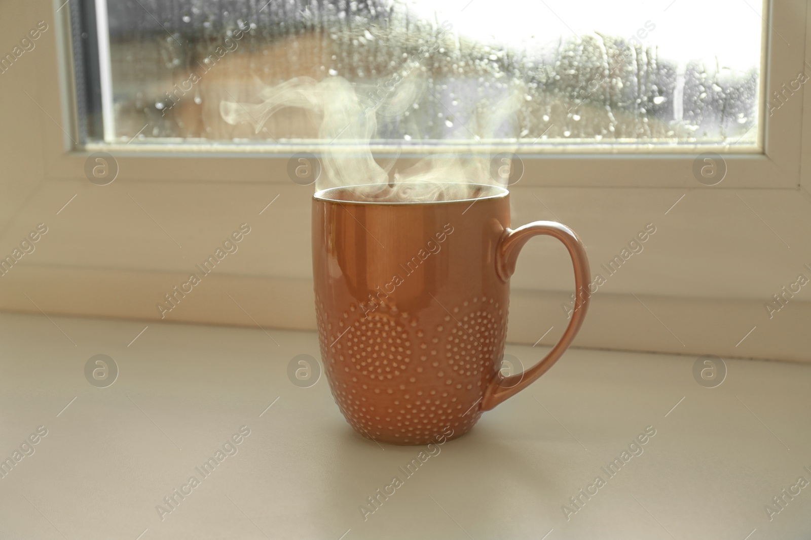 Photo of Cup of hot drink near window on rainy day