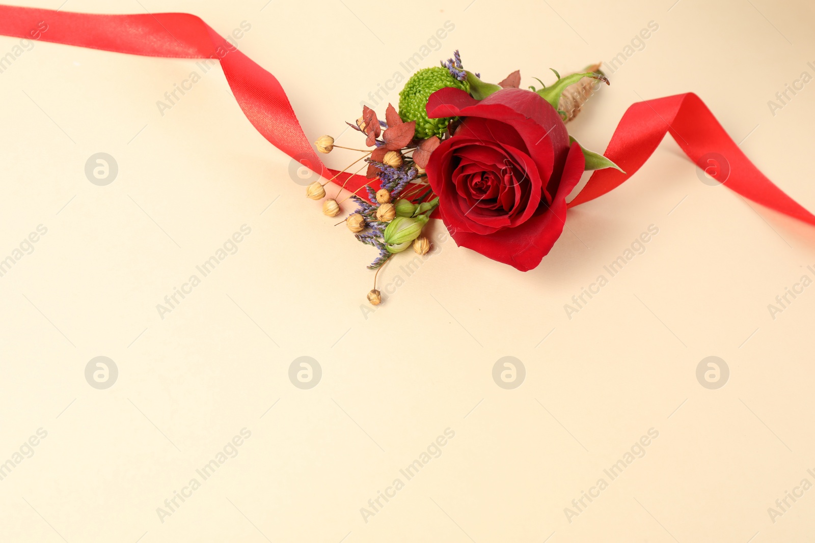 Photo of Stylish boutonniere with red rose and ribbon on beige background. Space for text