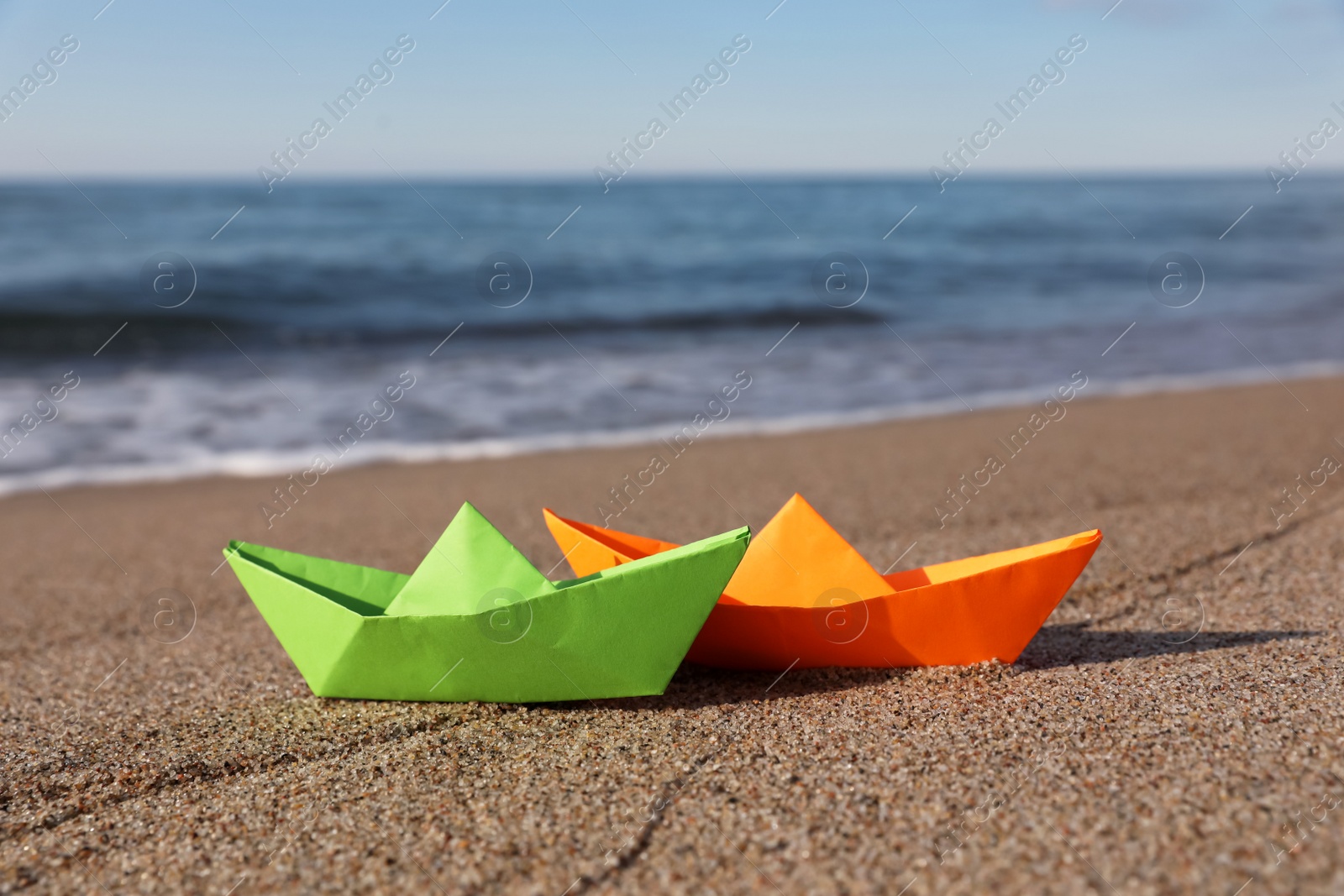 Photo of Bright color paper boats on sandy beach near sea