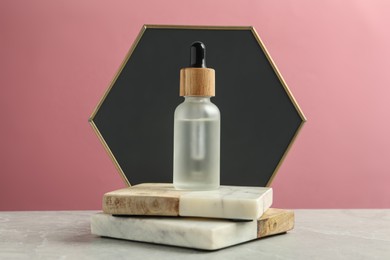 Photo of Bottle of face serum with marble boards on grey table against pink background