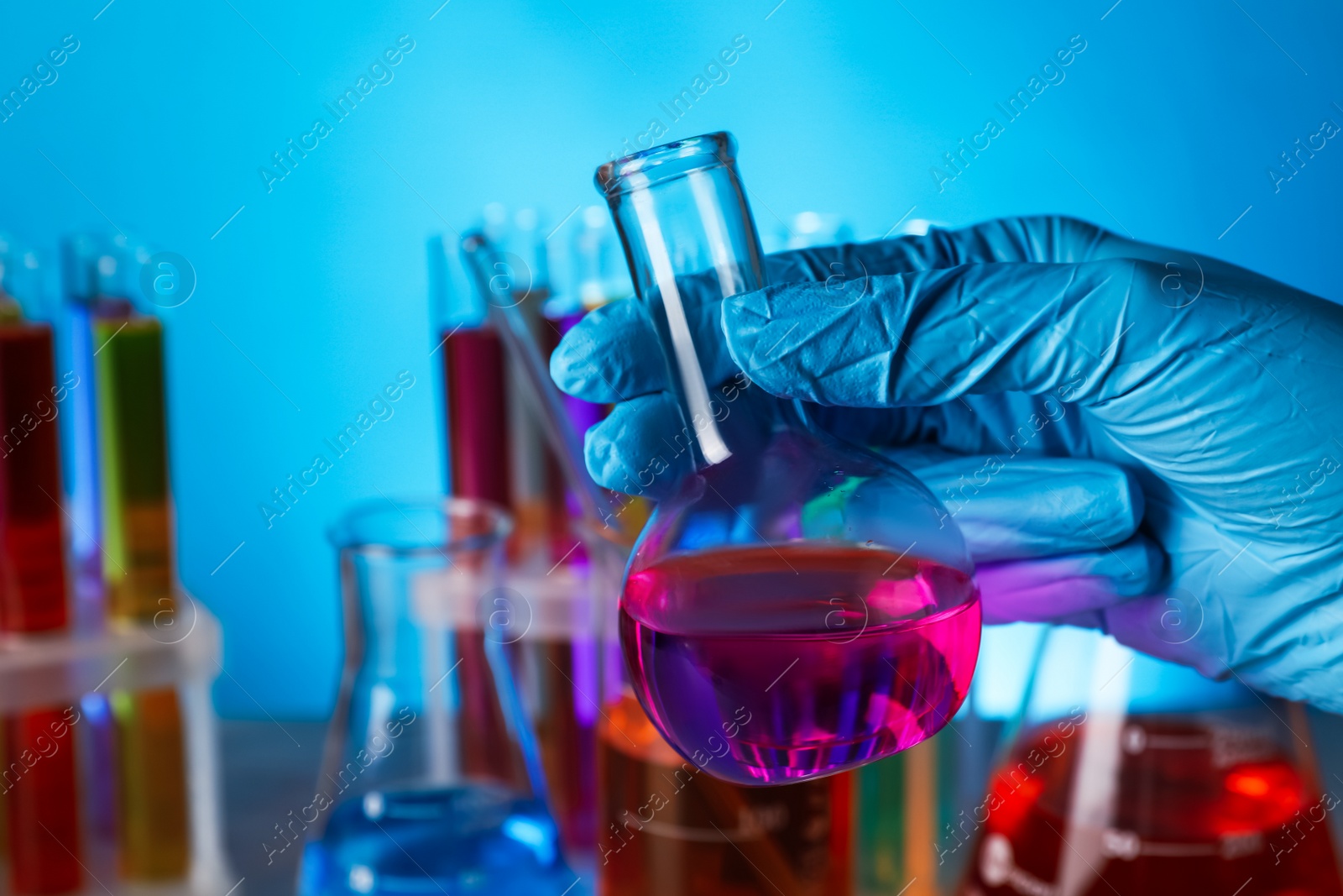 Photo of Scientist holding flask with liquid on light blue background, closeup