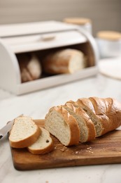 Wooden bread basket with freshly baked loaves and knife on white marble table in kitchen, closeup