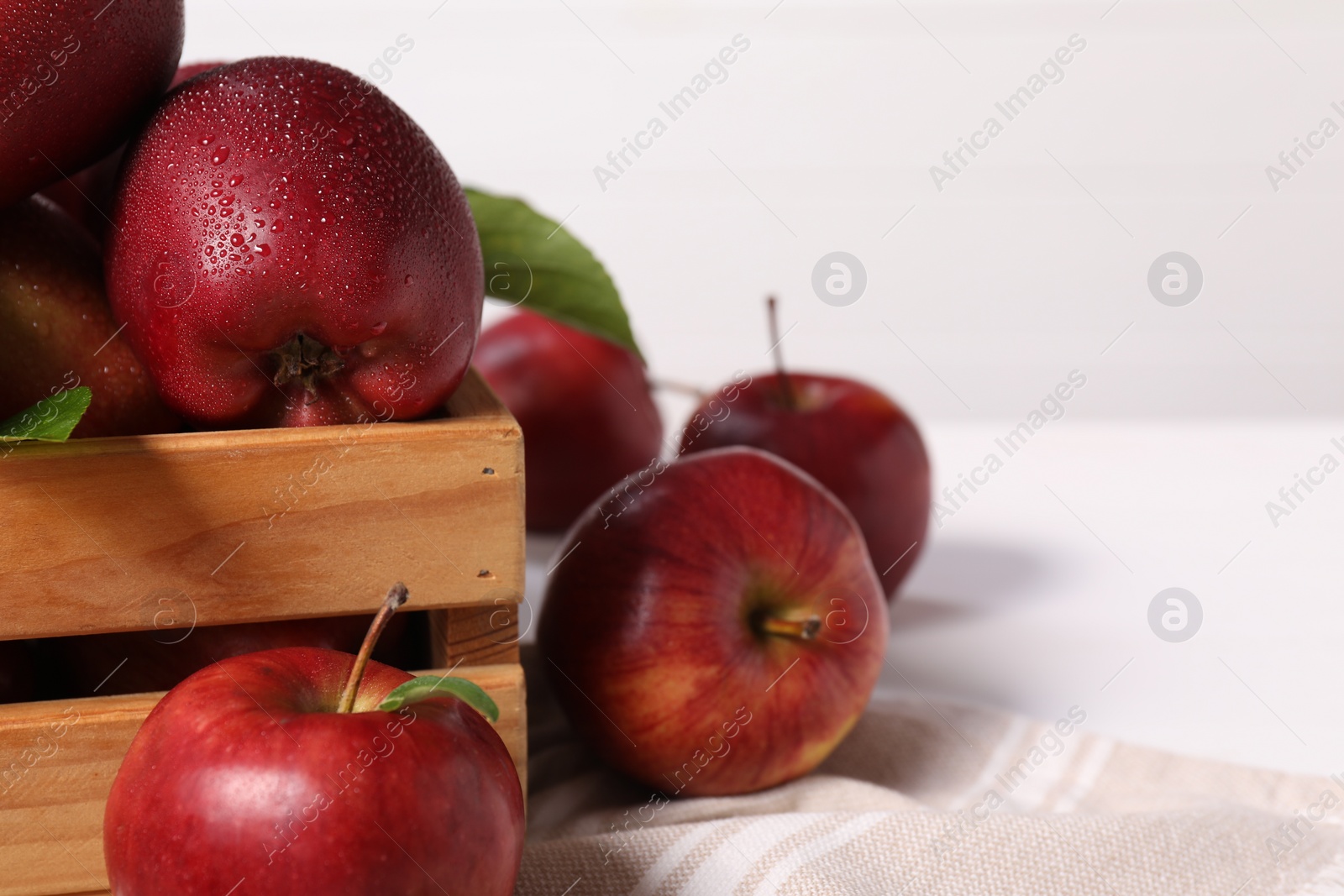 Photo of Fresh red apples in wooden crate on white table, closeup. Space for text