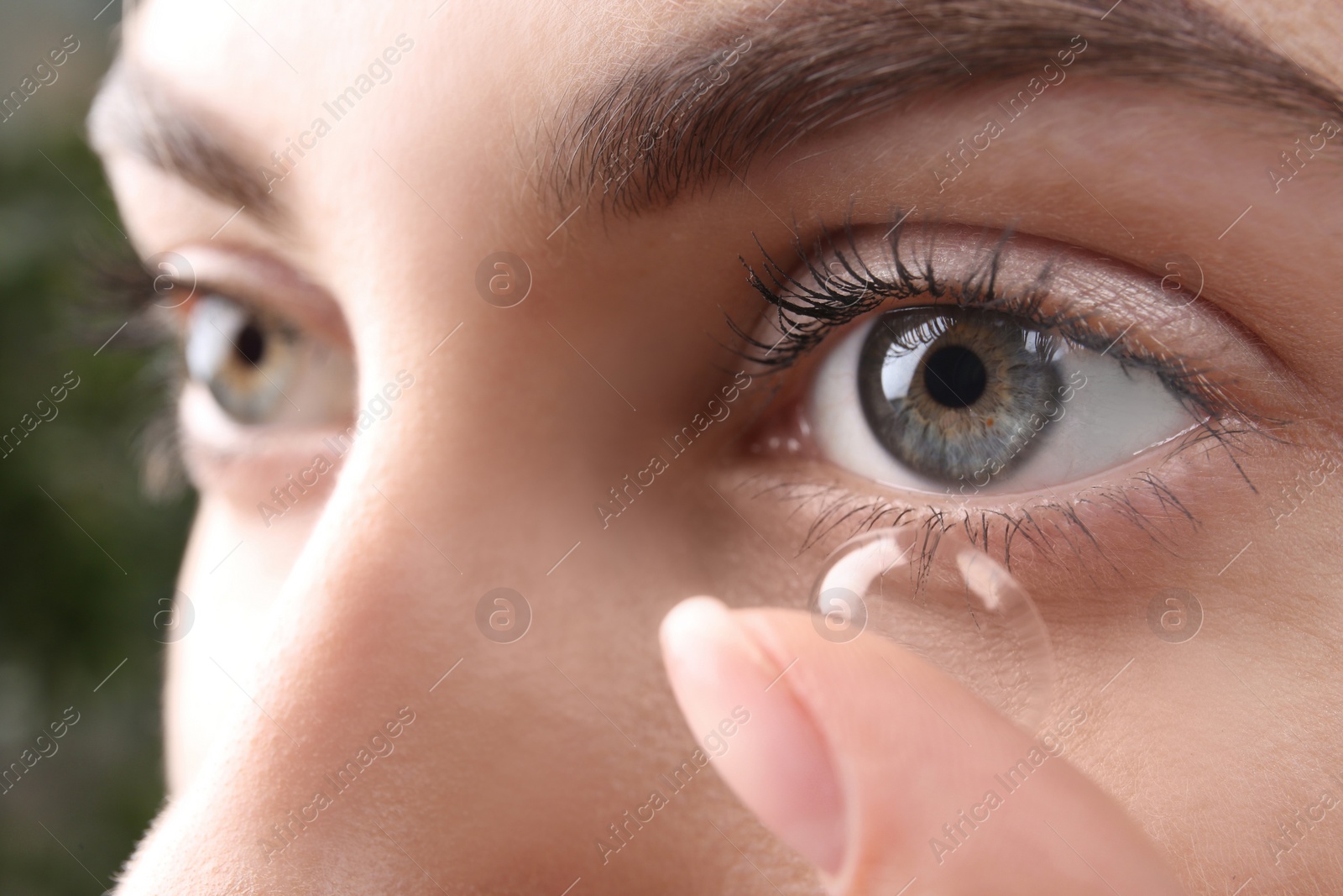 Photo of Young woman putting contact lens in her eye, closeup