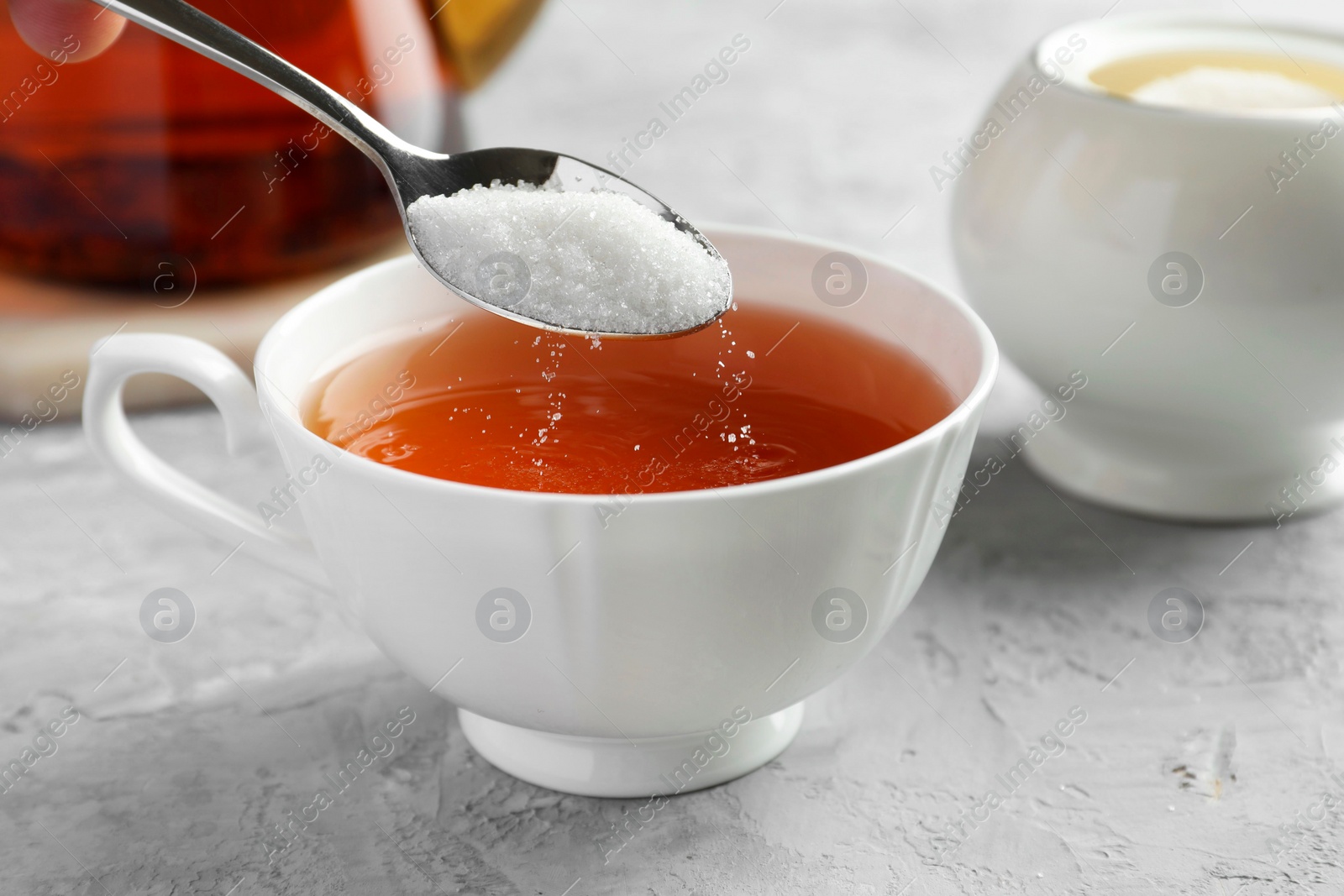 Photo of Adding sugar into cup of tea at grey textured table, closeup