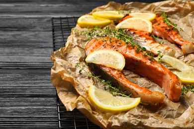 Photo of Tasty grilled salmon steaks, lemon slices and thyme on black wooden table, space for text