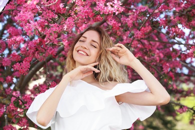 Attractive young woman posing near blossoming tree on sunny spring day