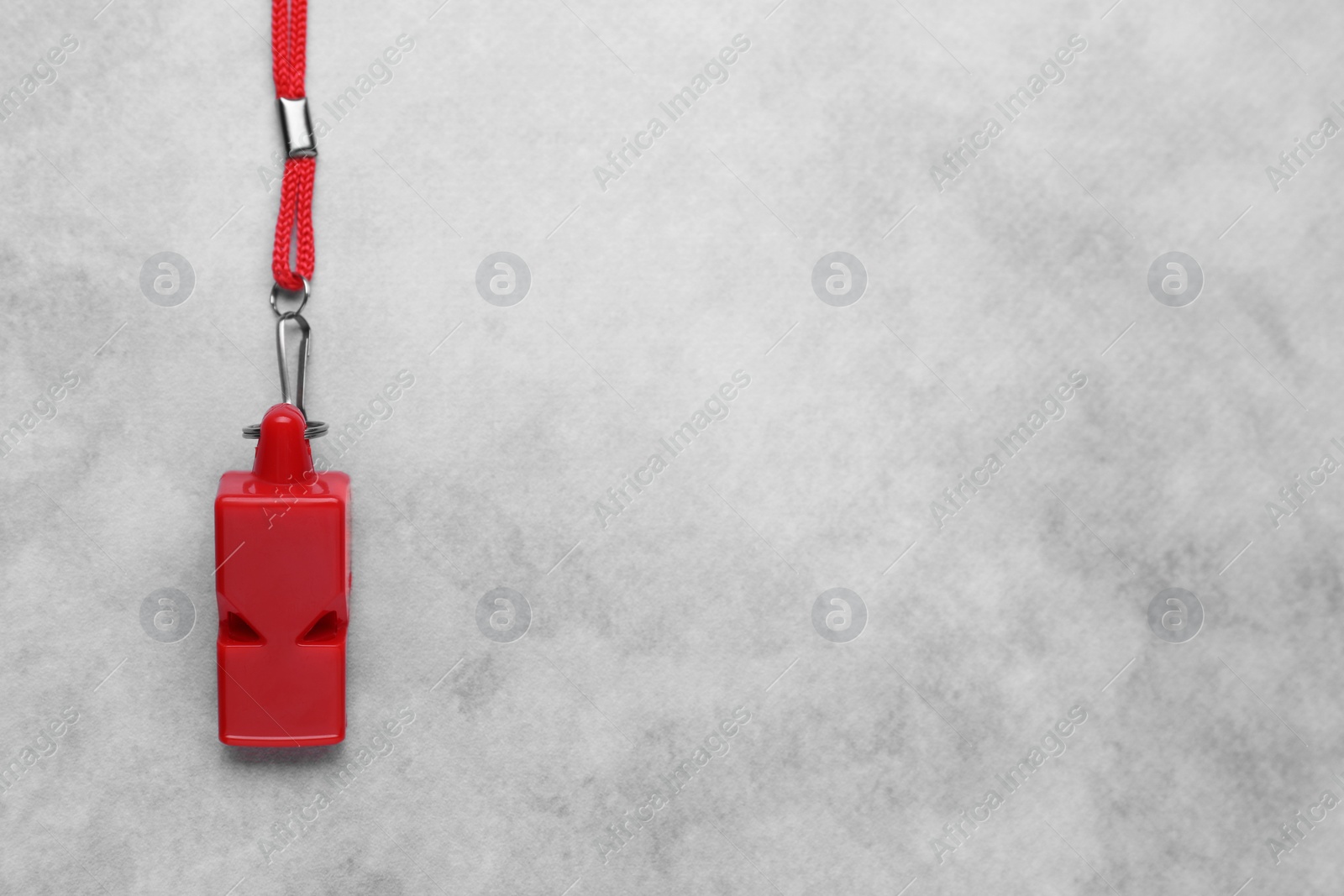 Photo of One red whistle with cord on light grey table, top view. Space for text