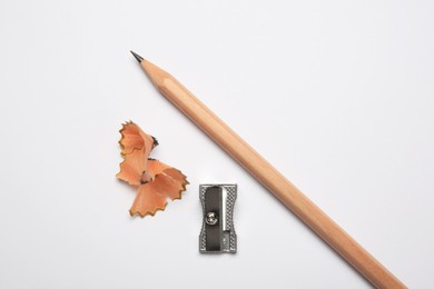Photo of Graphite pencil, sharpener and shavings on white background, flat lay
