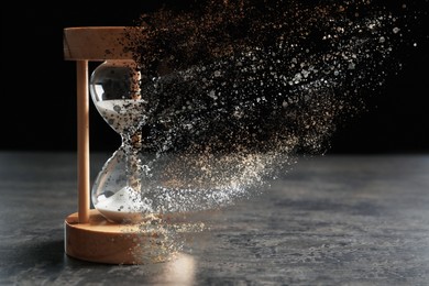 Image of Time is running out. Hourglass vanishing on grey table against black background