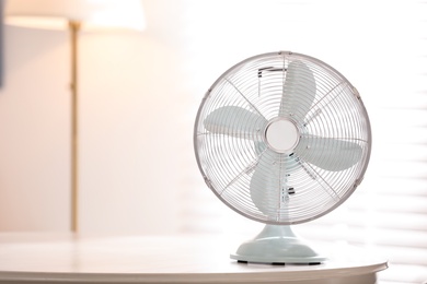 Photo of Modern electric fan on white table indoors. Space for text