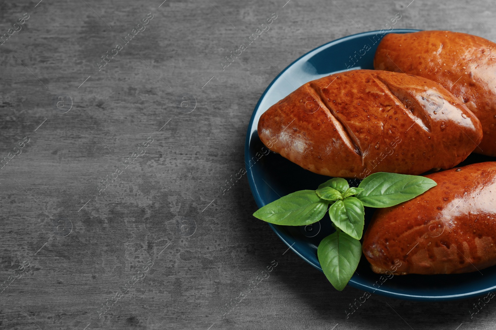 Photo of Delicious baked patties and basil on grey table. Space for text