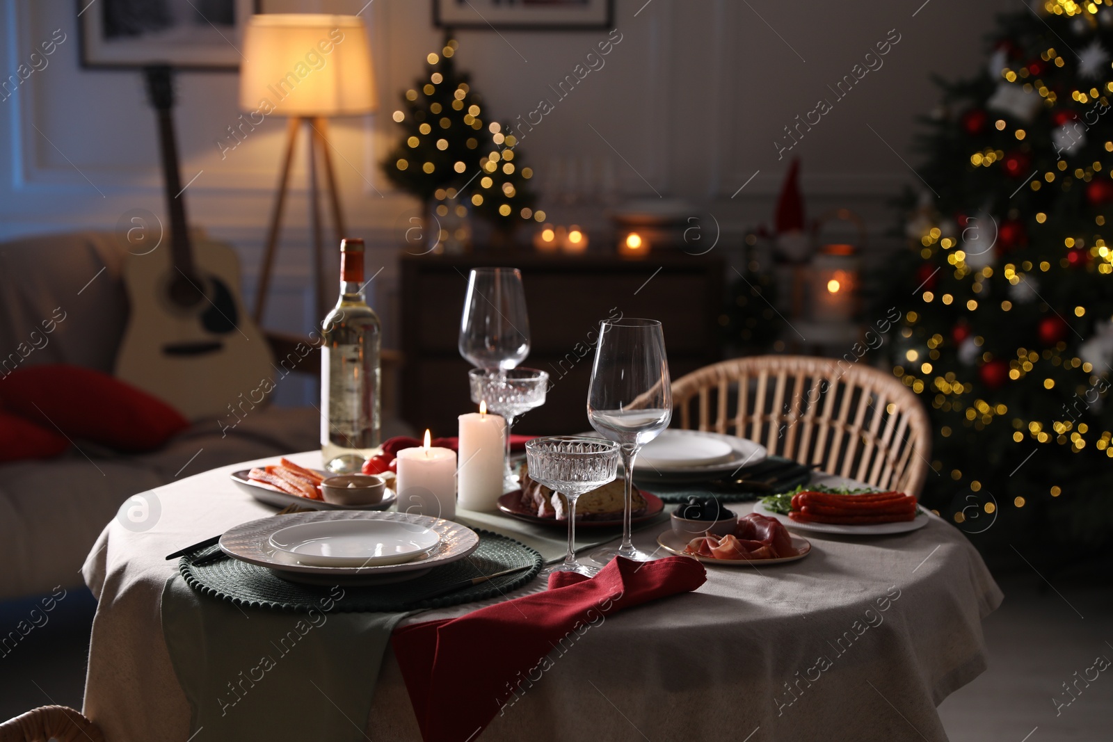 Photo of Christmas table setting with burning candles, appetizers and dishware in room