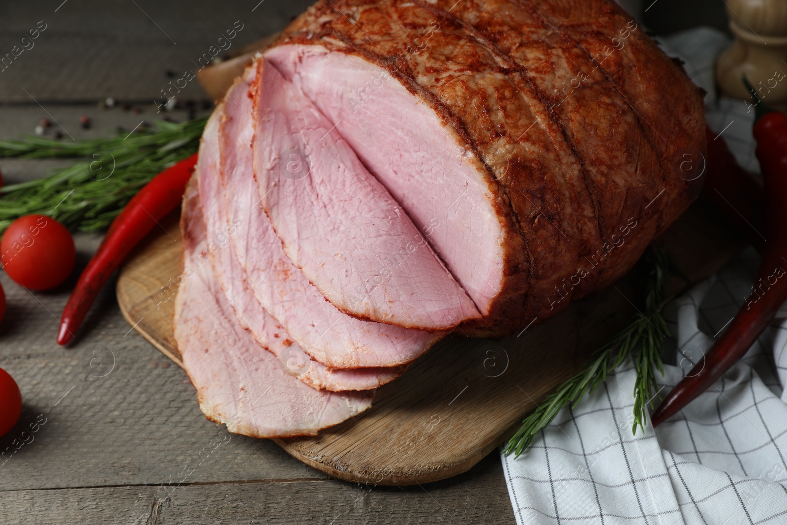 Photo of Delicious baked ham, tomatoes, chili peppers and rosemary on grey wooden table, closeup