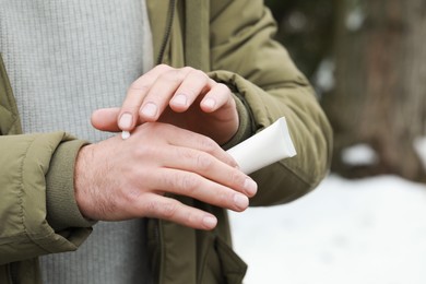 Man applying cream from tube onto hand outdoors, closeup. Winter care