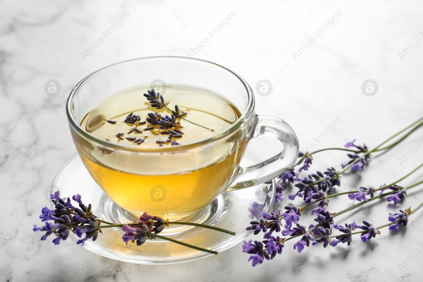 Photo of Fresh delicious tea with lavender and beautiful flowers on white marble table