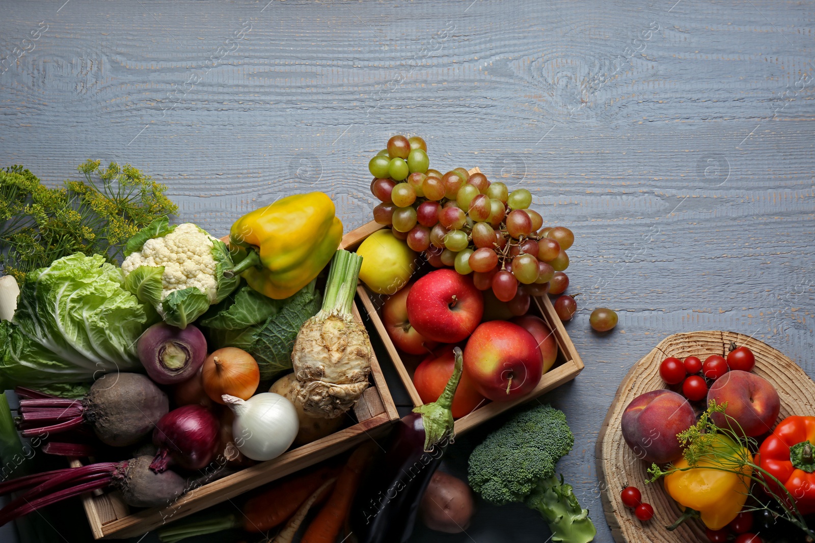 Photo of Different fresh vegetables and fruits in crates on grey wooden table, flat lay. Farmer harvesting