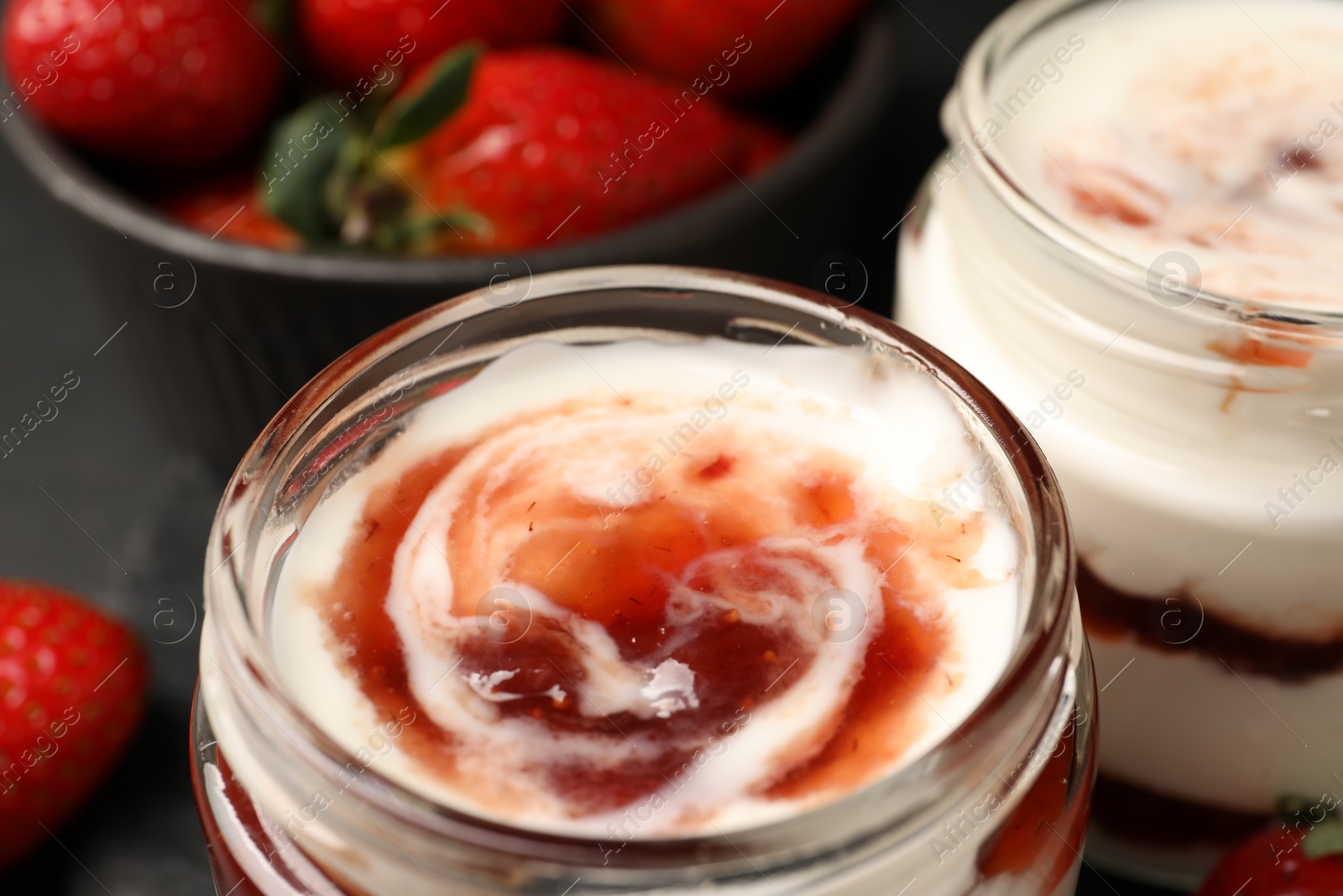 Photo of Tasty yoghurt with jam and strawberries on black table, closeup